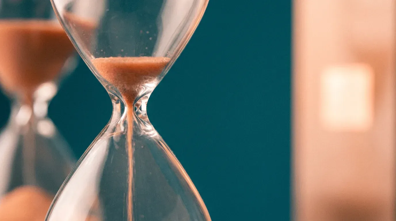 Primer plano de un reloj de arena con arena naranja sobre fondo teal
